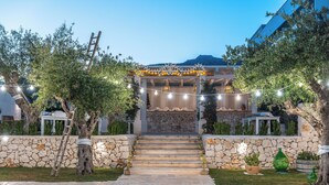 A stone staircase leading to a covered outdoor area with string lights, surrounded by trees and a stone wall.