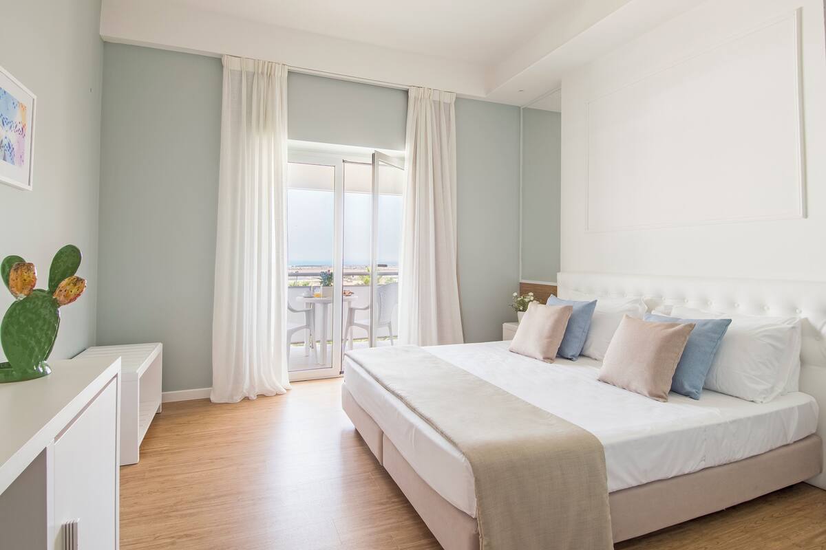 Un dormitorio con una cama grande, una mesita de noche, una silla y vistas al exterior.