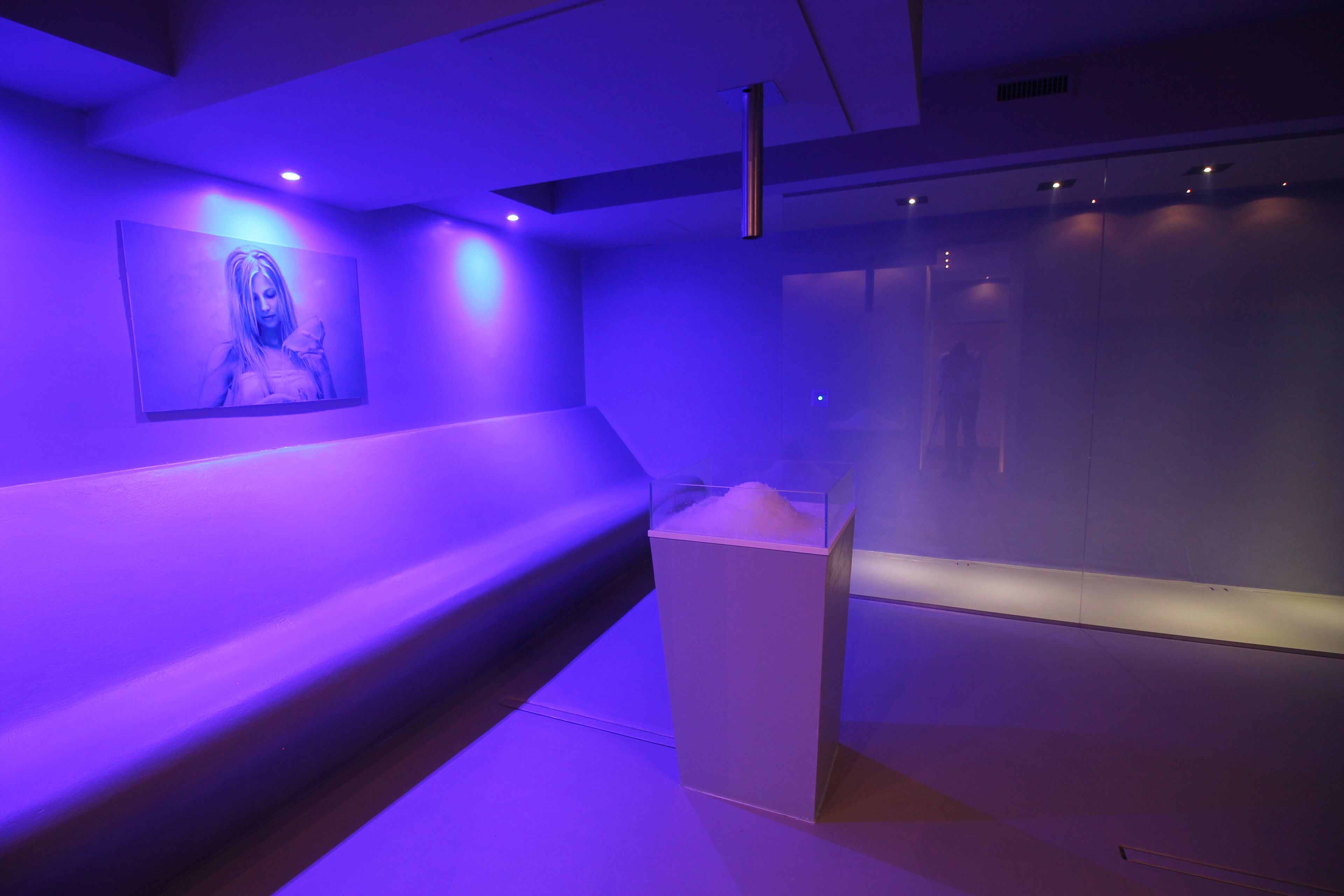 Een modern interieur met een blauw verlichte wand, een witte bank en een glazen vitrine.