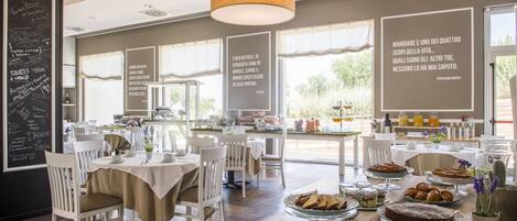 A dining area with tables set for breakfast, featuring various pastries and desserts.