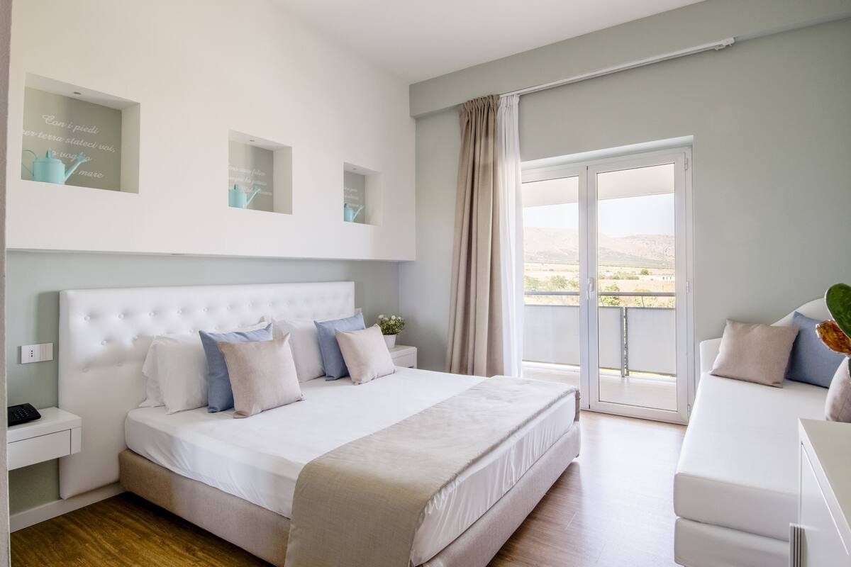 Un dormitorio con una cama grande, una mesita de noche, una ventana con cortinas y vistas al exterior.
