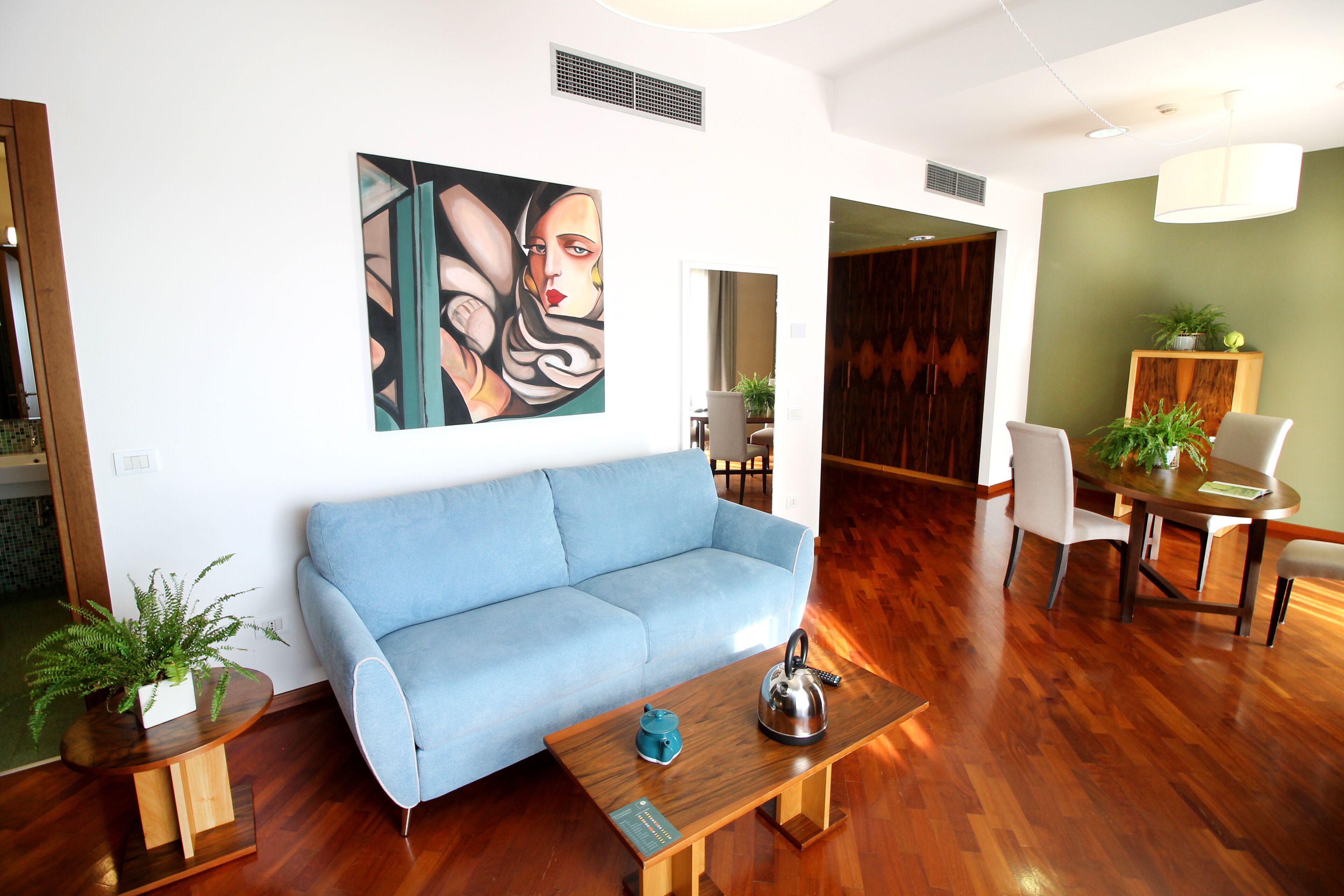 Een moderne woonkamer met een blauwe bank, een houten salontafel en een schilderij aan de muur.