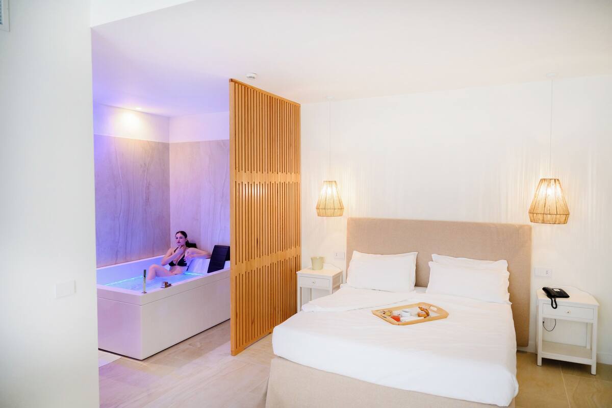 Una habitación de hotel moderna con una cama grande, un baño separado con bañera y dos lámparas de noche.
