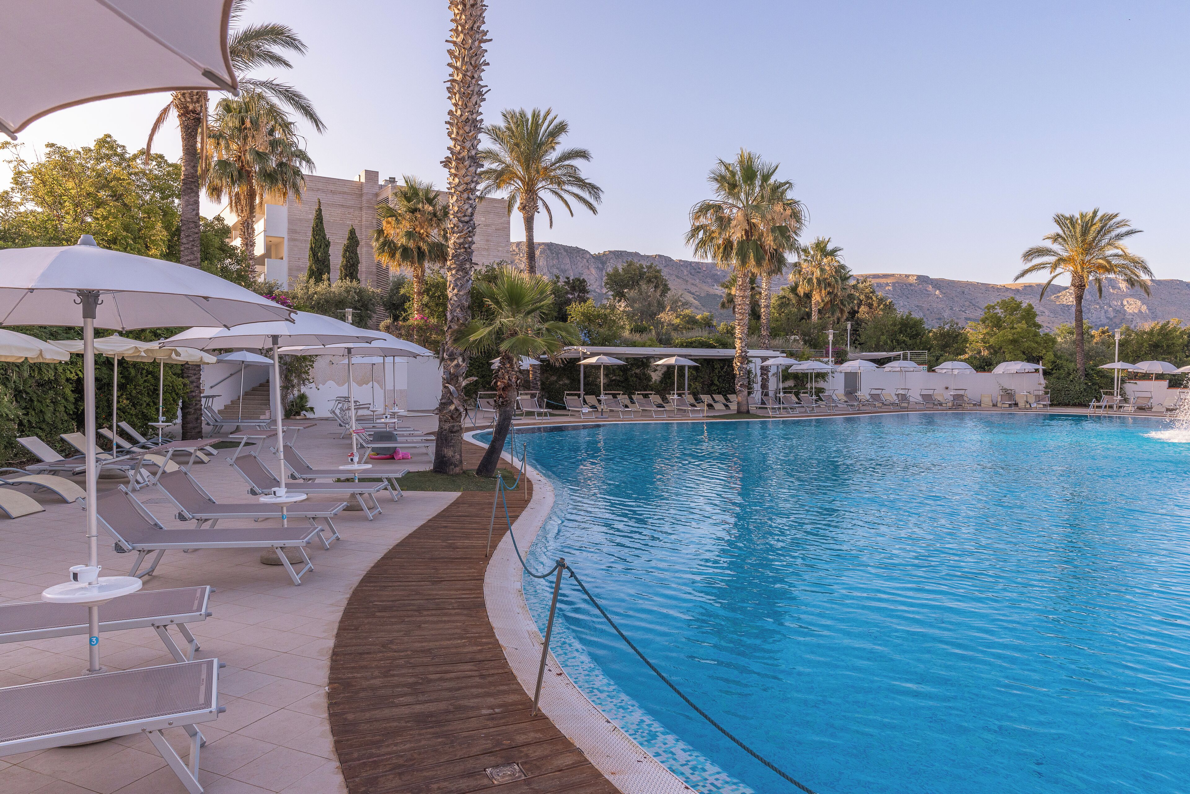 Zona de piscina con tumbonas, sombrillas y una terraza de madera.