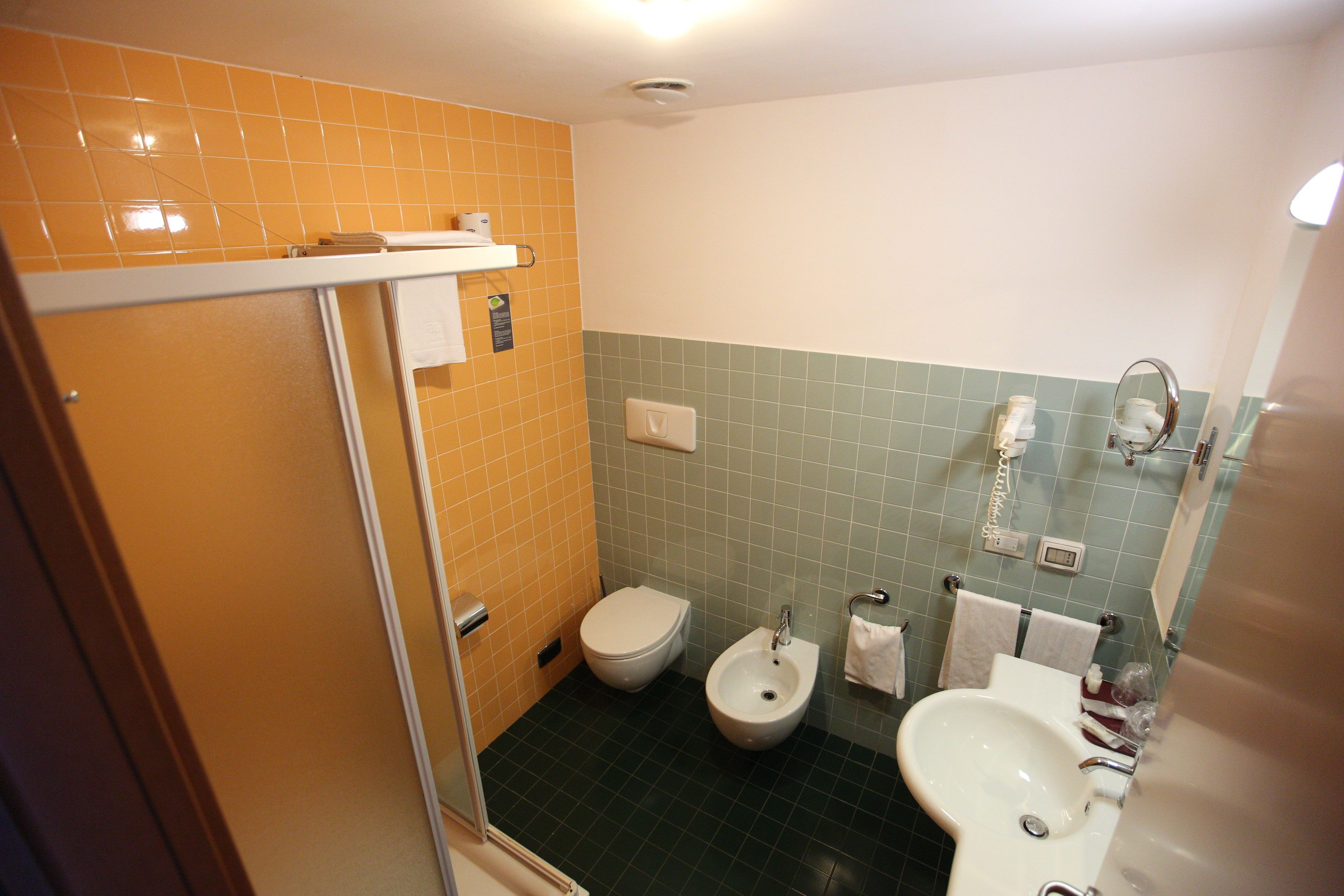 A bathroom with a toilet, bidet, and sink, featuring orange and green tiled walls.