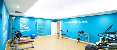 Un gimnasio con paredes azules, varios equipos de ejercicio y frases motivacionales.