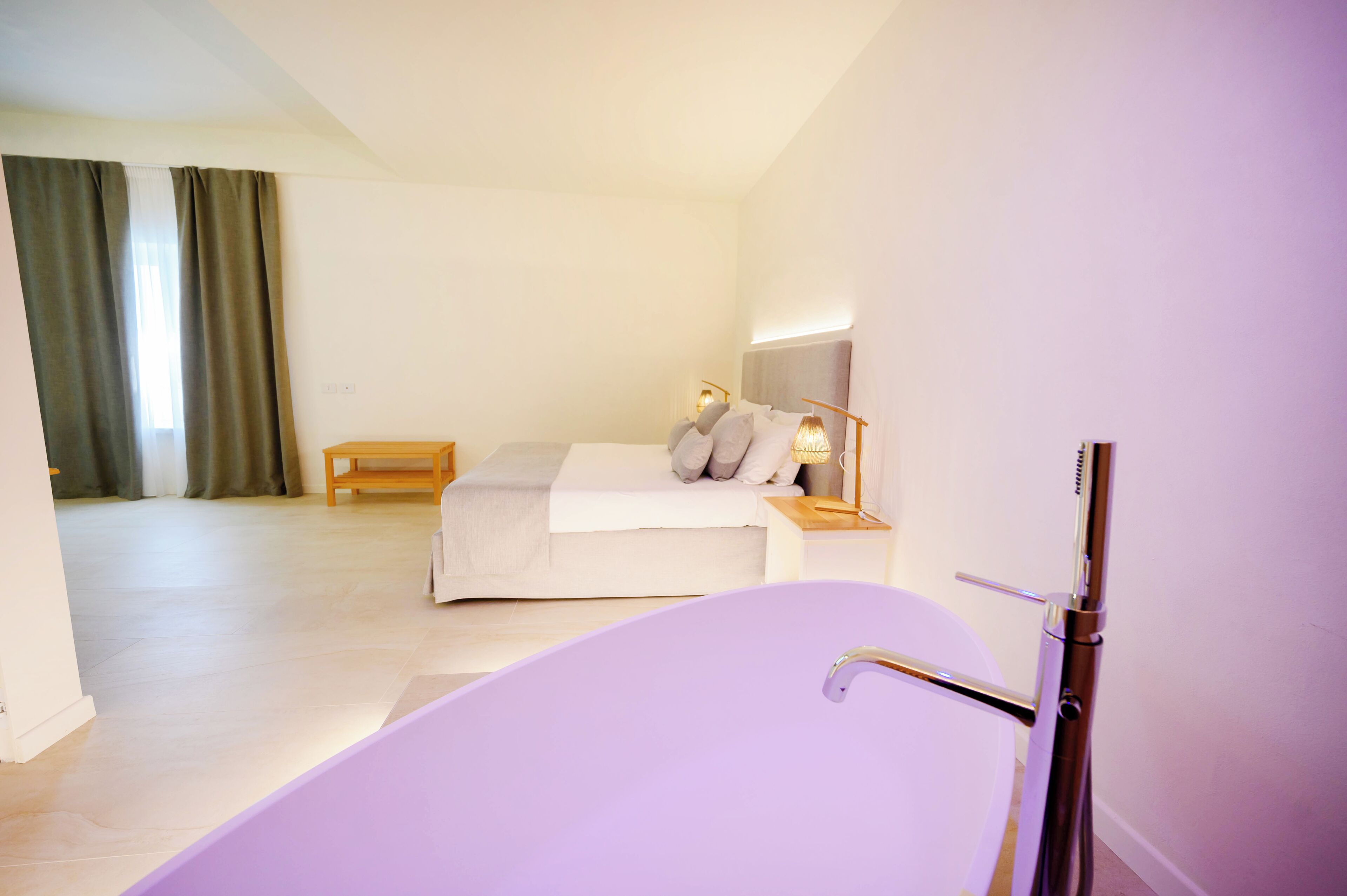 A modern bedroom with a bed, bedside table, lamp, and a large bathtub.