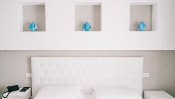A hotel room with a white bed, a nightstand with a phone, and three wall-mounted light fixtures.