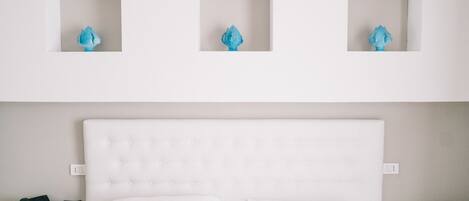 A hotel room with a white bed, a nightstand with a phone, and three wall-mounted light fixtures.