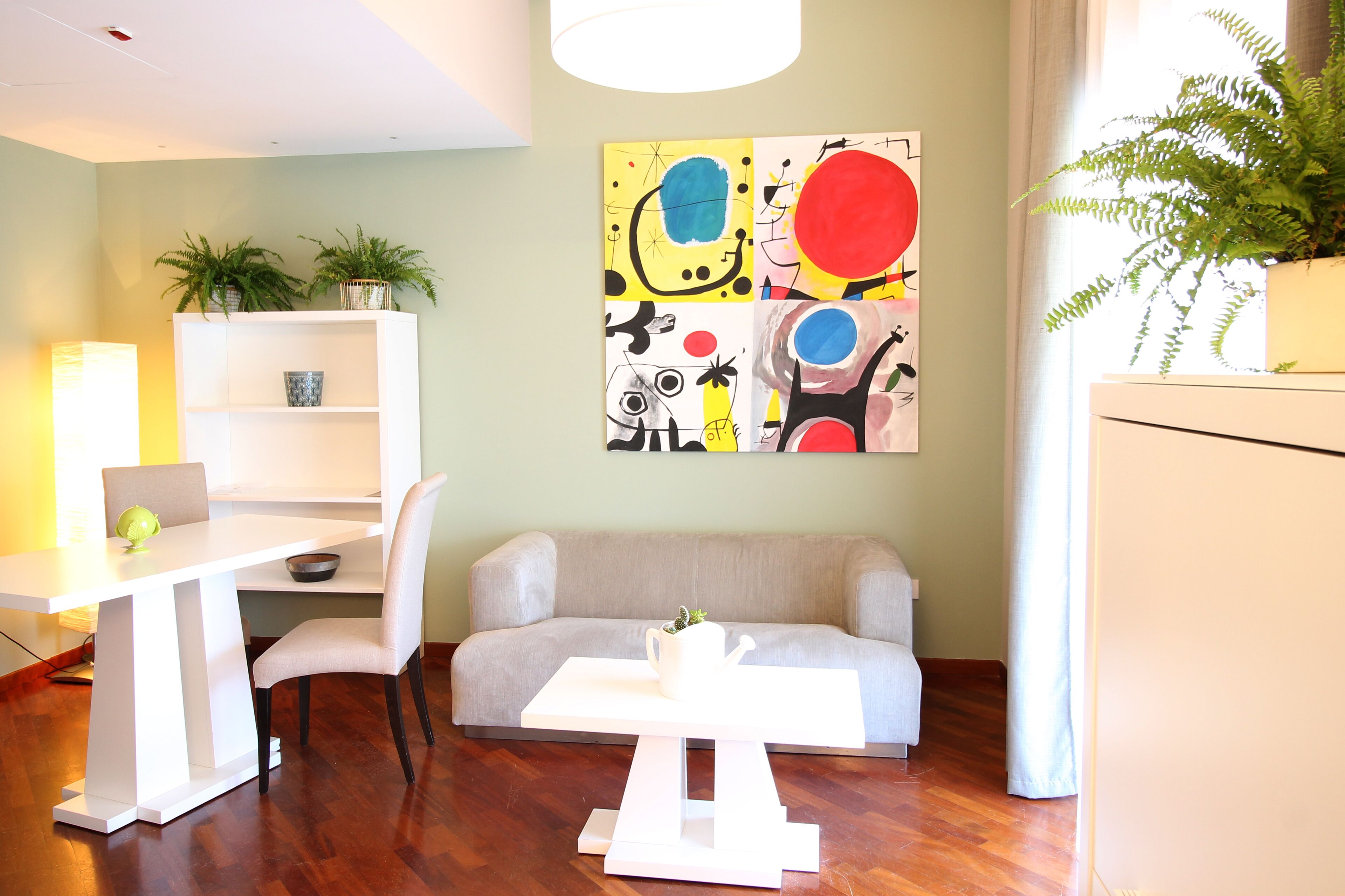 A modern living room with a white sofa, a dining table with a chair, a white coffee table, and a painting on the wall.