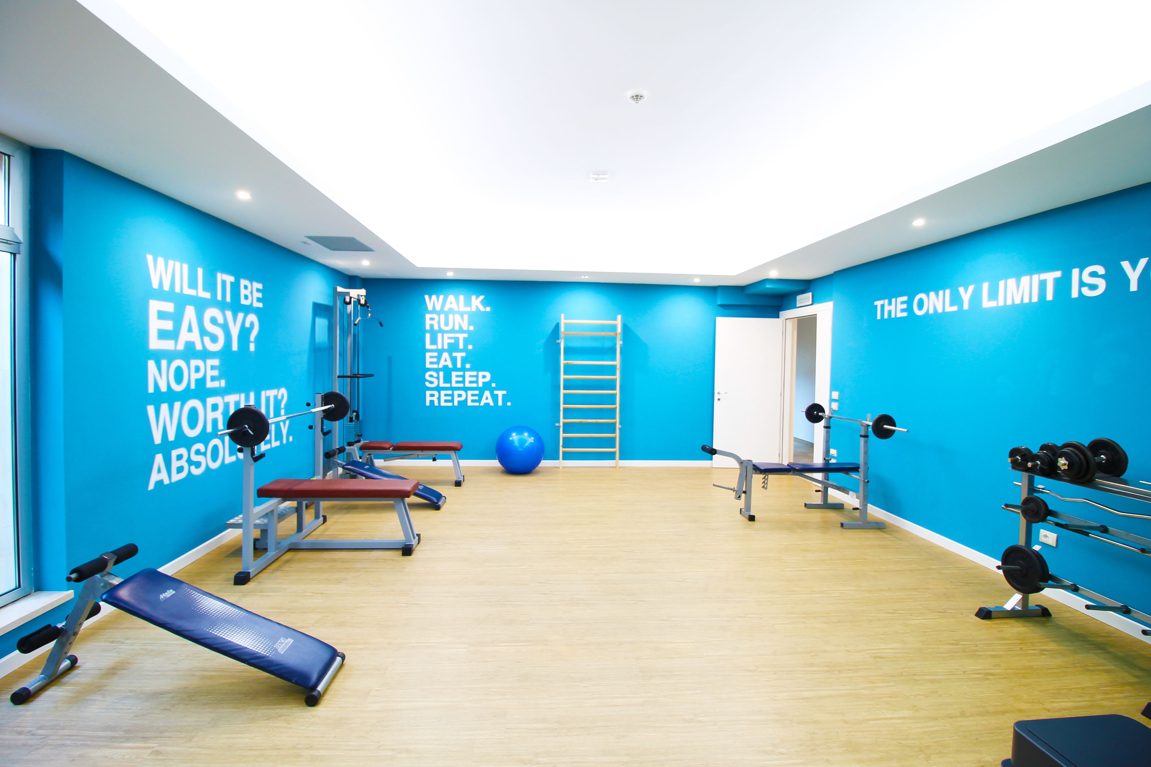 Un gimnasio con paredes azules, piso de madera y diverso equipo de ejercicio.