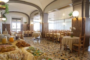 Un comedor con varias mesas y sillas, un bufé con distintos alimentos, y un suelo de baldosas.