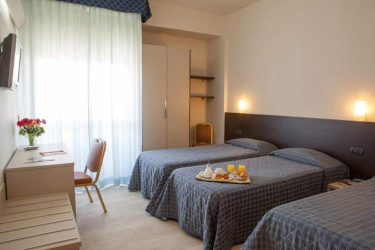 A hotel room with two single beds, a desk with a chair, a small table with breakfast, and a TV on the wall.