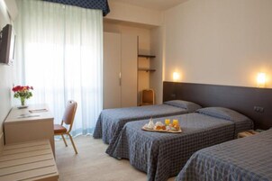 Habitación de hotel con dos camas individuales, un escritorio con silla, una pequeña mesa con desayuno y un televisor en la pared.
