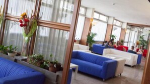 Eine moderne Hotelhalle mit blauen Sofas, Topfpflanzen und großen Fenstern.