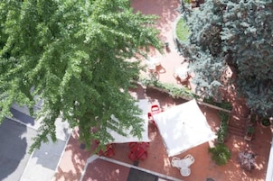 Vista aérea de un patio con sillas rojas, un paraguas blanco y un árbol.