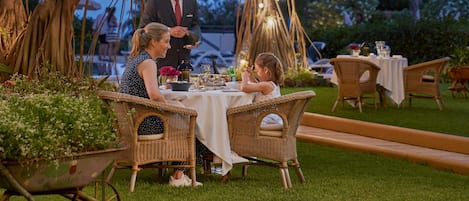 An outdoor dining area with a table set for two under a tree adorned with string lights.