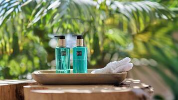 A wooden table with two bottles of hand and body lotion and a bowl with a white towel.