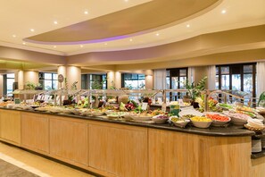 A buffet with a variety of food options, including salads, fruits, and other dishes, arranged on a long counter with a wooden finish. - Porto Mare Hotel, by PortoBay (Funchal)