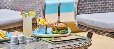 Une table à manger avec un hamburger, des frites et une boisson, le tout installé devant une piscine.
