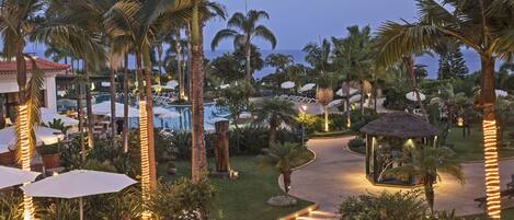 A resort with outdoor seating, palm trees, a pool, and a gazebo.