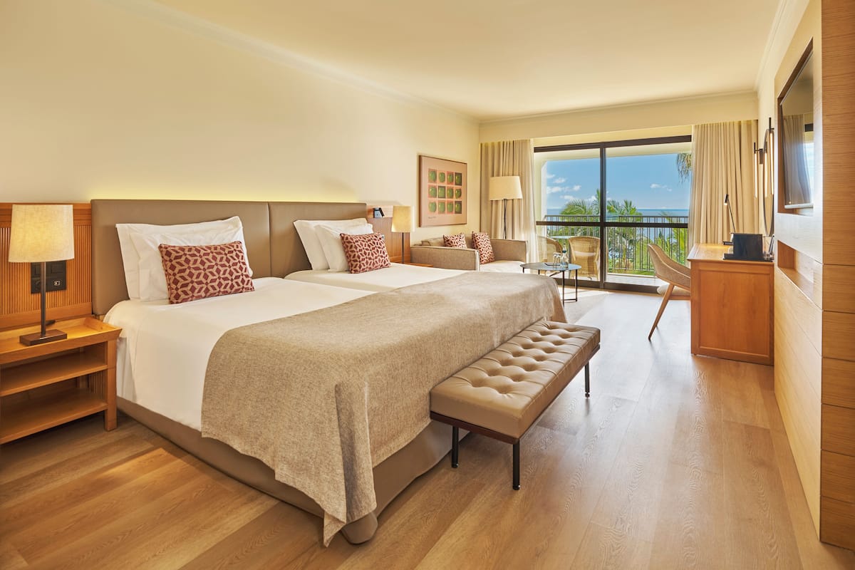 A hotel room with a large bed, a bench, a desk, and a balcony with a view.