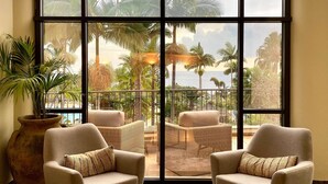 A room with two armchairs, a round coffee table, and a large window with a view of palm trees and a pool. - Porto Mare Hotel, by PortoBay (Funchal)