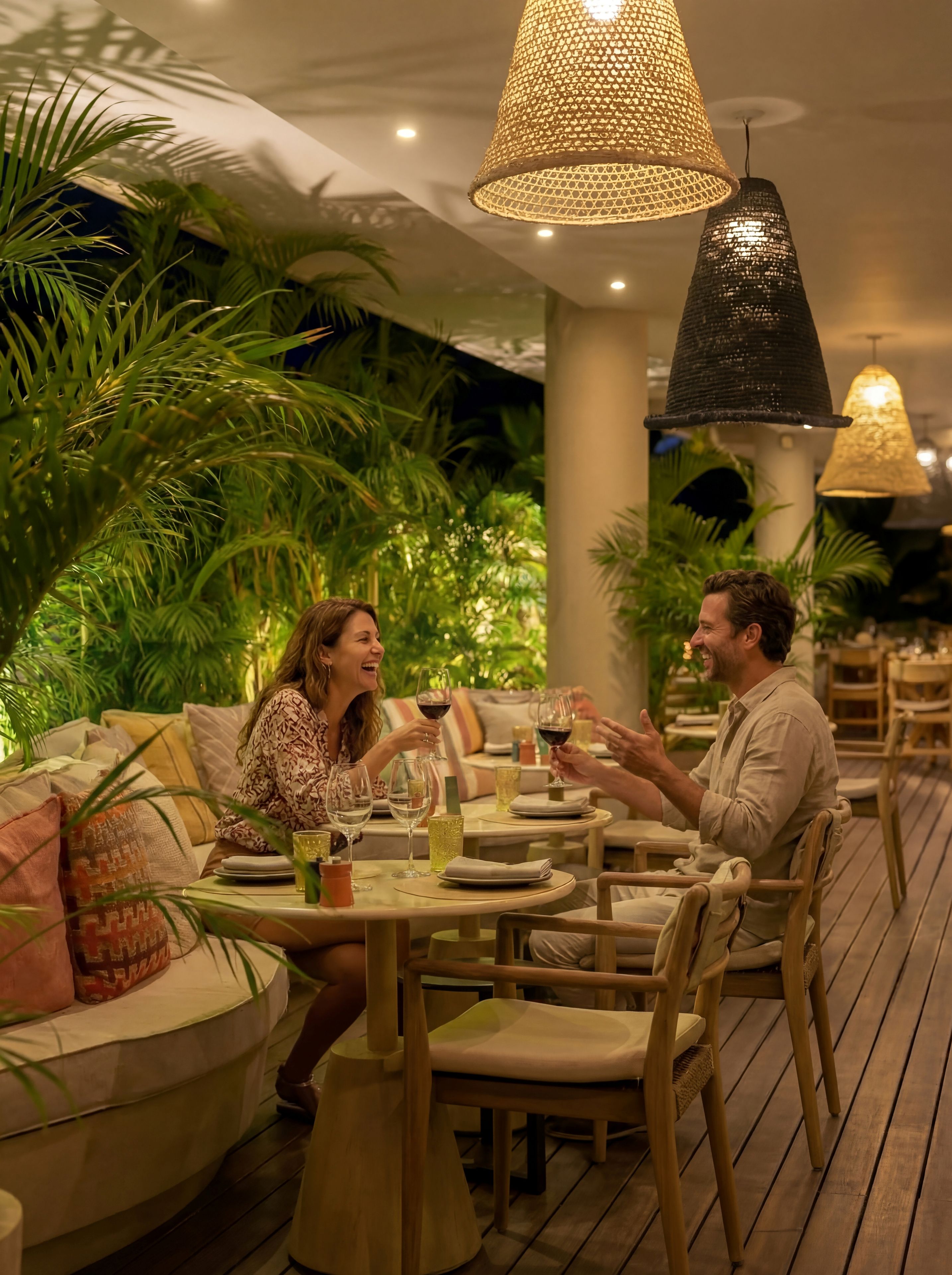 Una pareja cenando en una mesa con vista a plantas de interior, rodeada de mobiliario de madera e iluminación colgante.