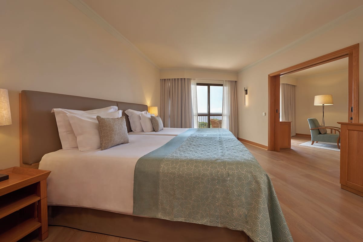 A hotel room with a large bed, a wooden nightstand, a chair, and a view of the balcony.