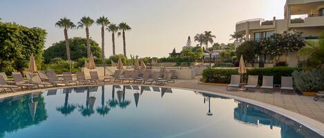 Una piscina con sillones de descanso y palmeras.