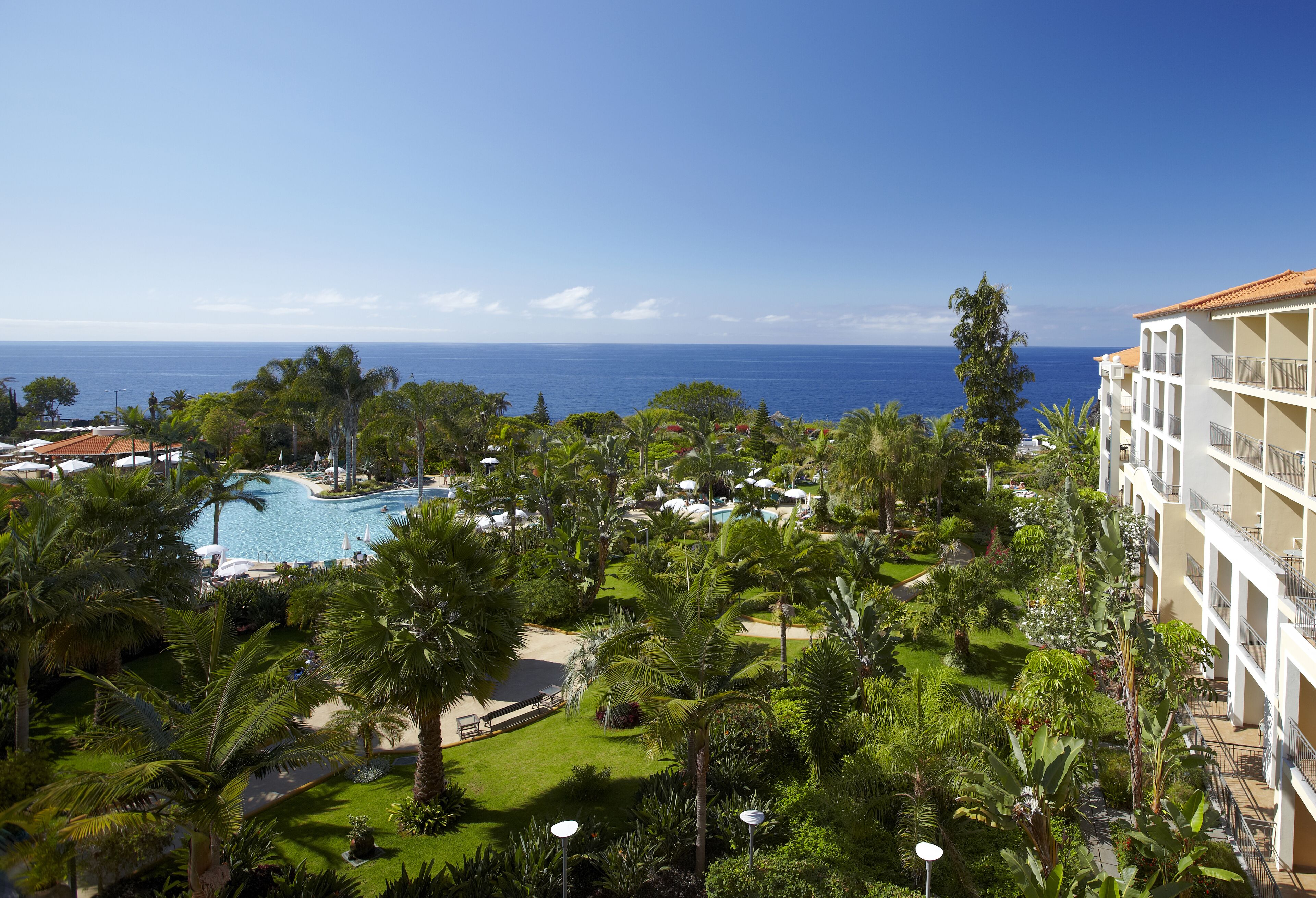 Ett semesterhotell med en swimmingpool, frodig grönska och utsikt över havet.