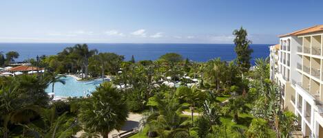 A resort with a swimming pool, lush greenery, and a view of the ocean.
