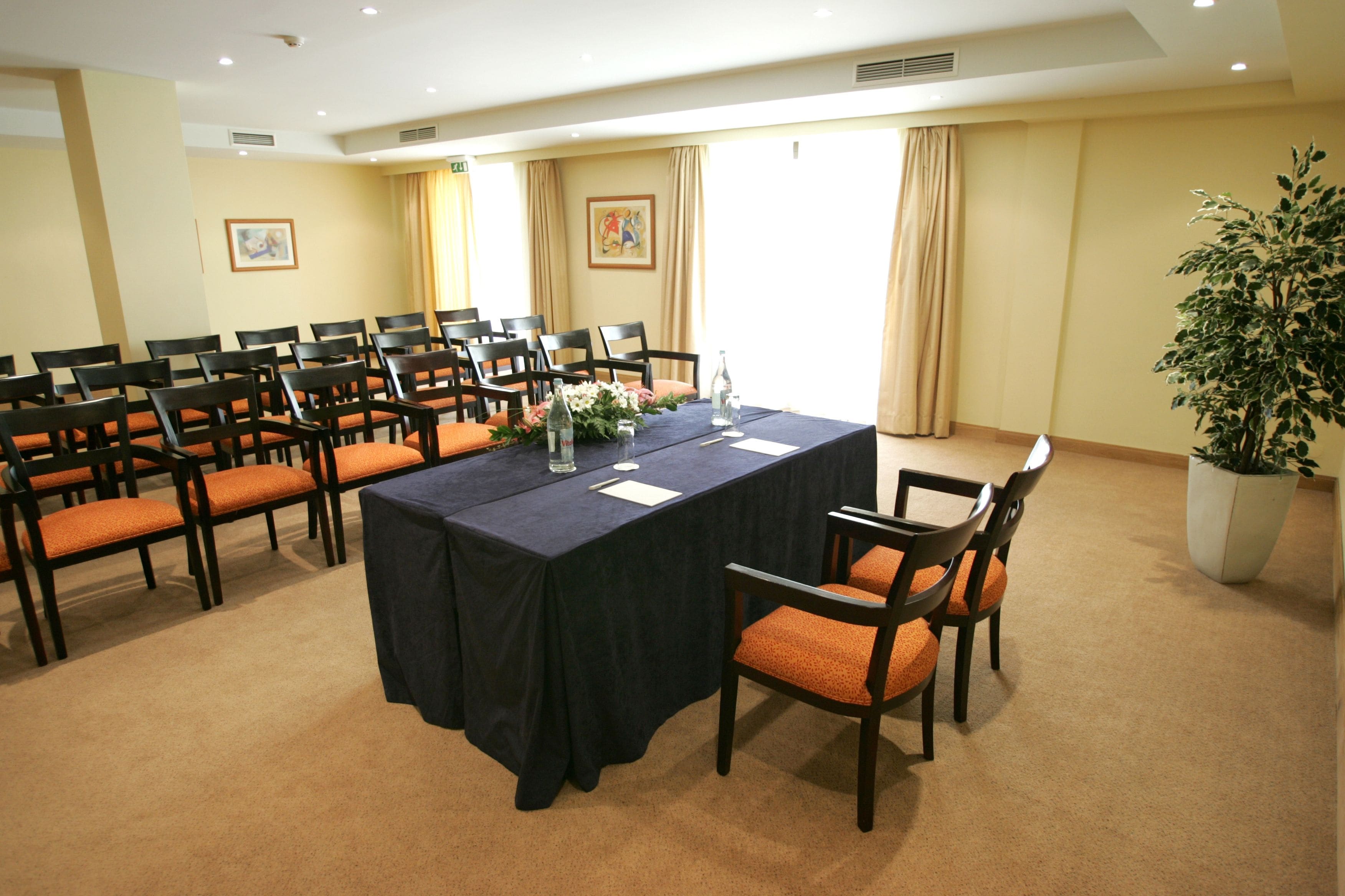 Un salón de conferencias con una larga mesa, sillas y una planta en maceta.