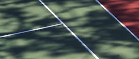 A tennis court with a shadow of a person on the green surface.