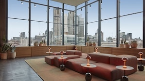 A modern interior with large windows, a sectional sofa, and multiple potted plants. - One Hundred Shoreditch (London)