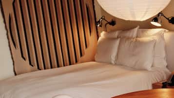 Una cama bien hecha con sábanas blancas, una mesa redonda de madera con un mantel individual y un gran farol de papel blanco colgando arriba.