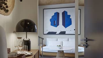 A modern bedroom with a bed, a wall-mounted abstract painting, a bedside table with glasses and a kettle, and a view of the room's ceiling.