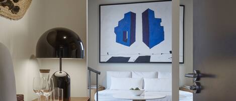 A modern bedroom with a bed, a wall-mounted abstract painting, a bedside table with glasses and a kettle, and a view of the room's ceiling.