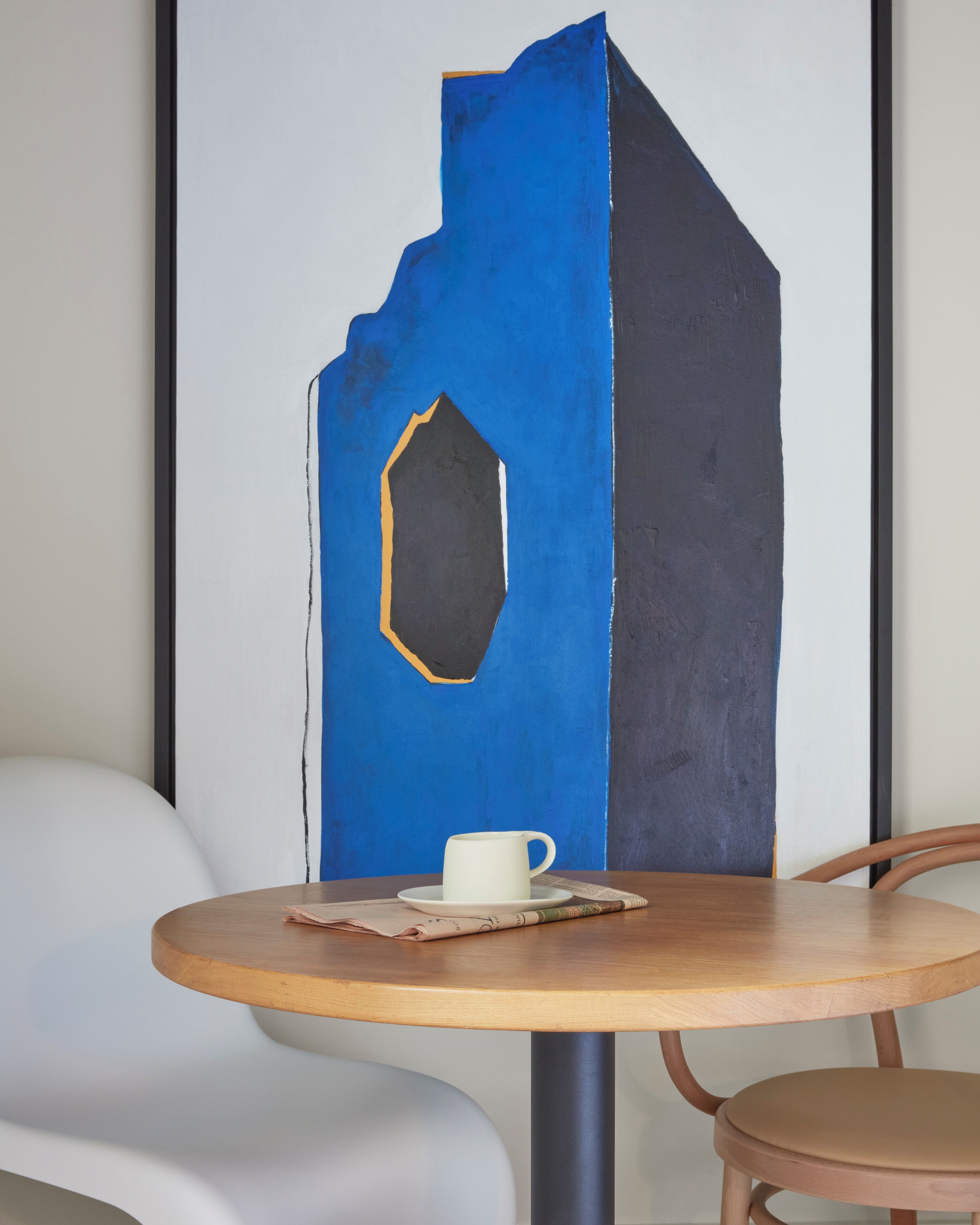 Una mesa redonda de madera con una taza blanca y un periódico.