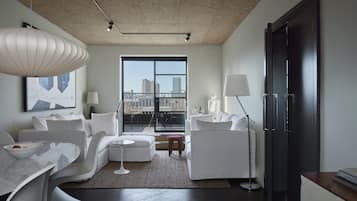A modern living room with a sofa set, a dining table, and a large window offering a city view.