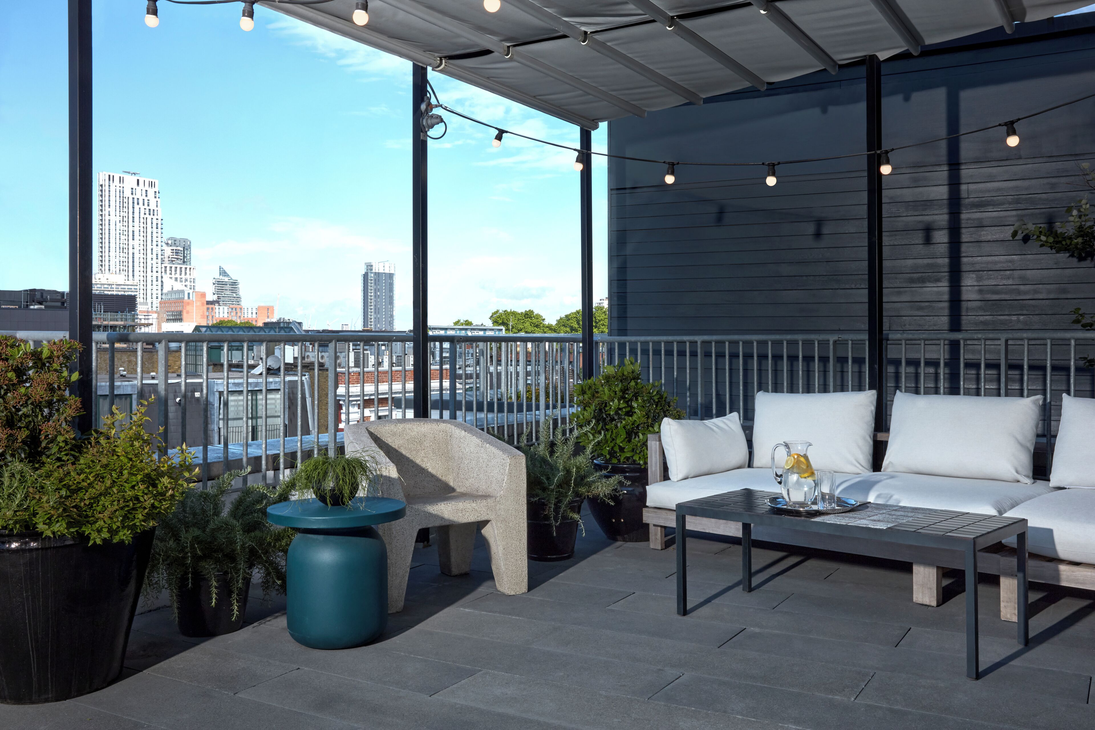 A rooftop terrace with a sofa, coffee table, and potted plants.