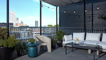 Terraço no telhado com sofá, mesa de centro e plantas em vasos.