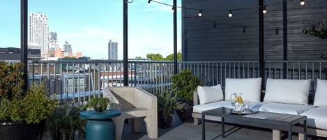A rooftop terrace with a sofa, coffee table, and potted plants.