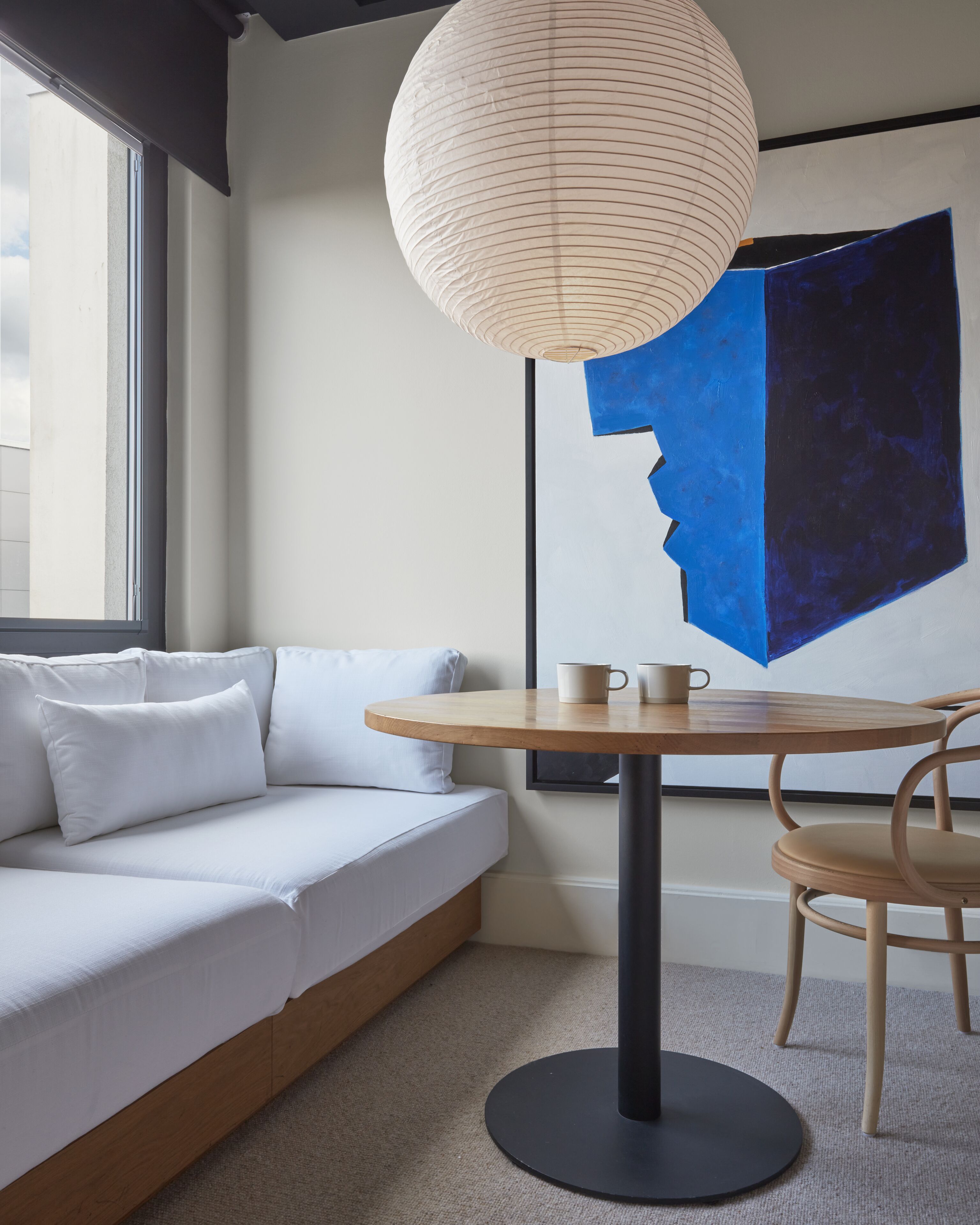 A modern room with a white sofa, a round wooden table with two cups, and a large abstract painting on the wall.