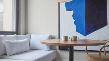 A modern room with a white sofa, a round wooden table with two cups, and a large abstract painting on the wall.