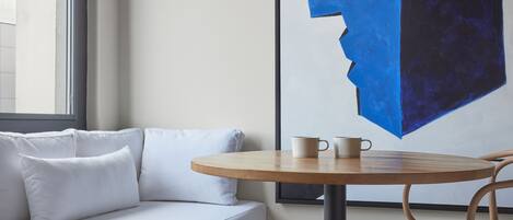 A modern room with a white sofa, a round wooden table with two cups, and a large abstract painting on the wall.