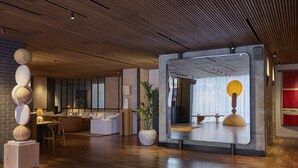 A modern interior with a wooden ceiling, a large mirror reflecting a room, a potted plant, and a seating area with a sofa and a table. - One Hundred Shoreditch (London)