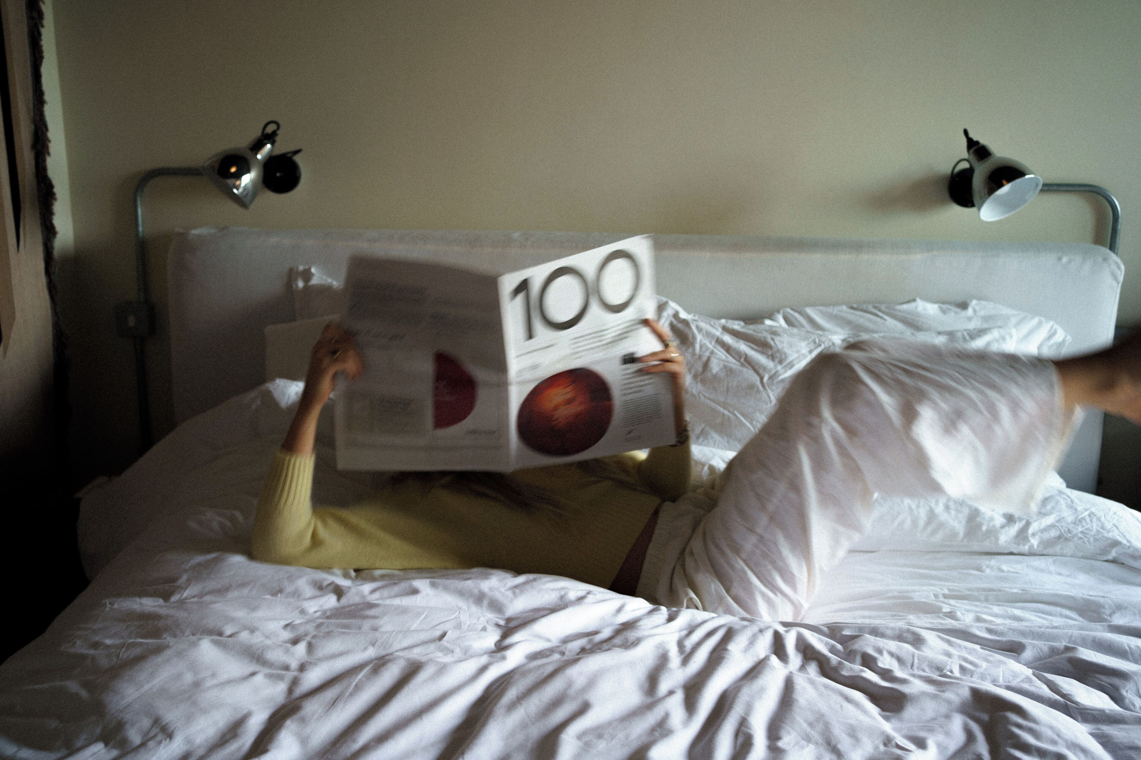 Iemand ligt in bed met een boek getiteld '100' over het gezicht.