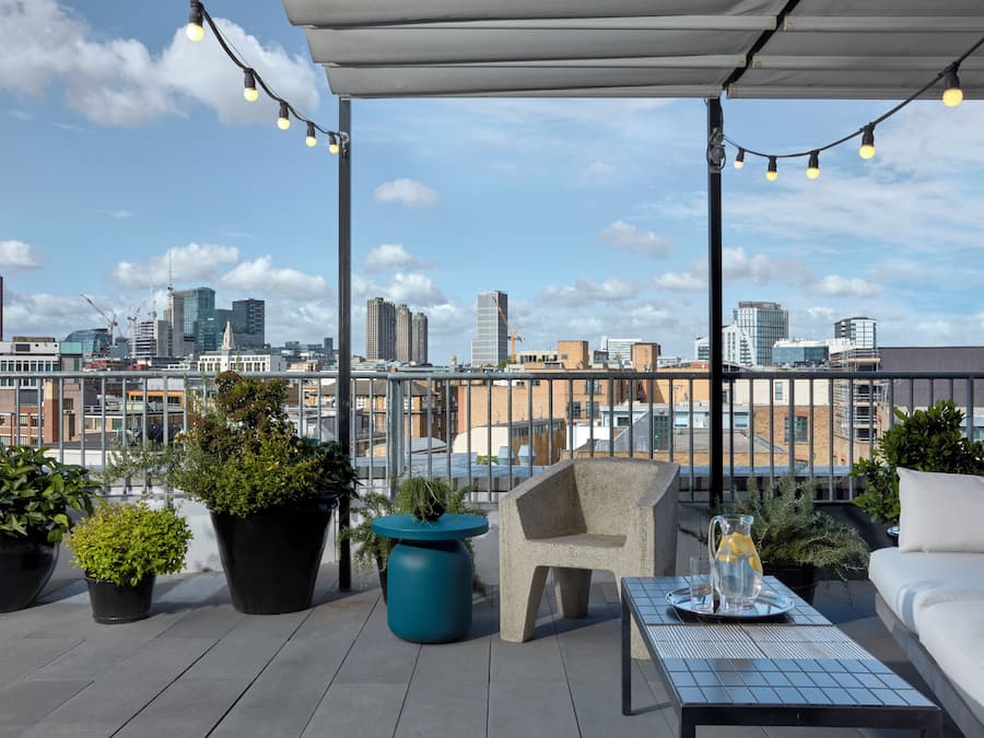 A rooftop terrace with potted plants, a seating area, and a city view.