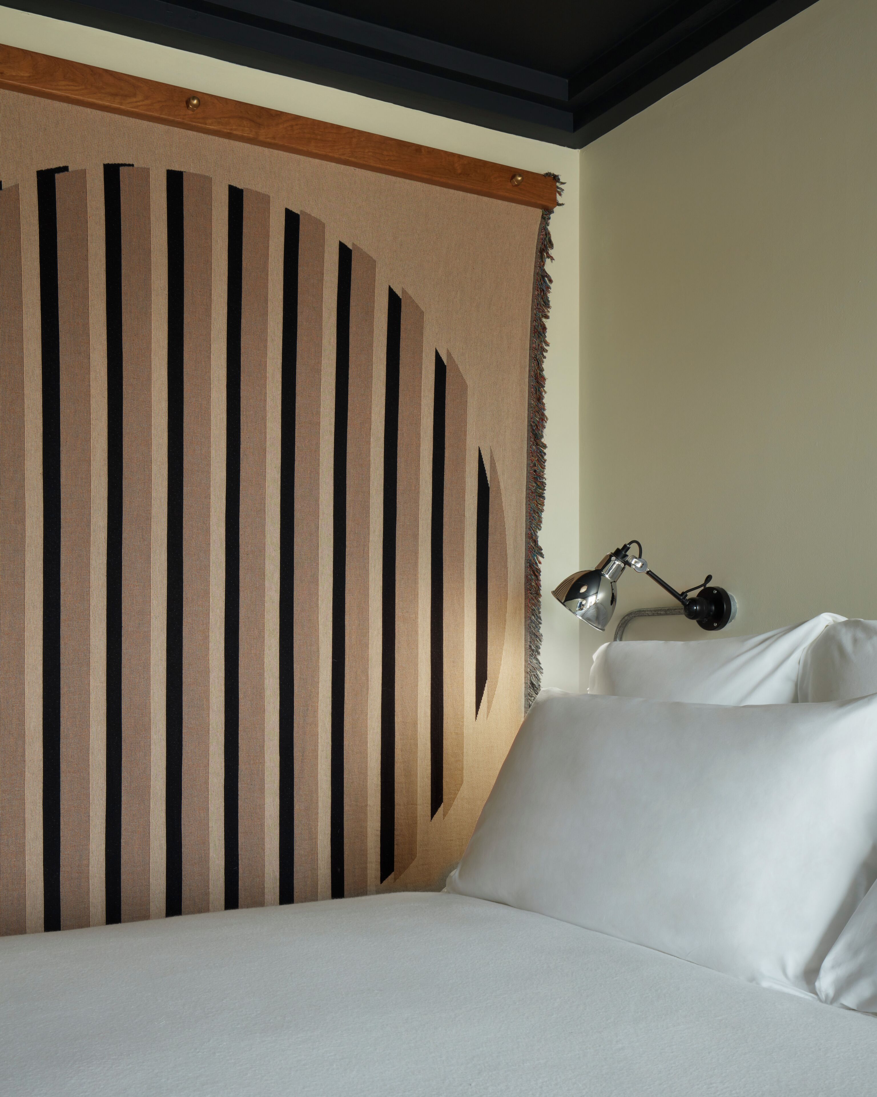Un lit avec du linge de lit blanc, une tête de lit avec des lattes de bois verticales et une lampe de chevet.
